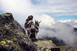 Woman with her rescue dog on top of a mountain above the clouds